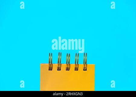 Closeup of yellow spiral notepad placed on bright blue background representing concept of office supplies Stock Photo