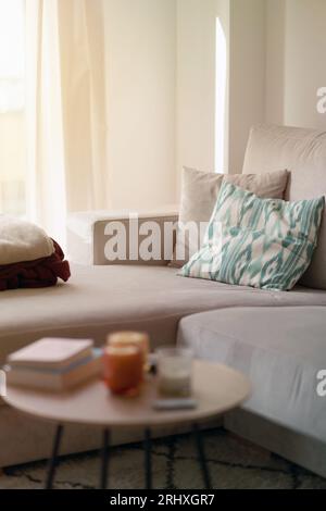 Candle lights reading books fan remote controller placed on round table near blurred comfortable sofa with pillows blankets in daylight Stock Photo