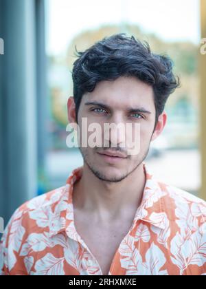 Head and shoulders shot of one handsome young man with green eyes in urban setting, looking at camera, wearing t-shirt Stock Photo