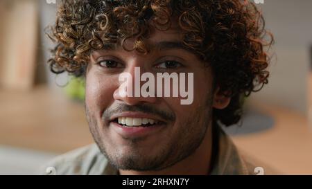 Close up smiling Arabian man homeowner with curly hair vlogger look at camera at kitchen. Portrait Indian male face with smile indoors. Headshot Stock Photo