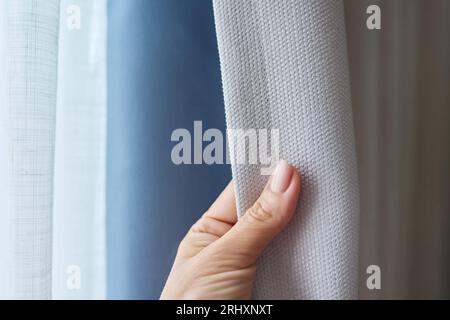 Woman's hand showing light gray curtain on blue opaque lining, fabric blackout Stock Photo