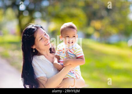 Mother and son in sunny park. Loving Asian family playing outdoor. Mom holding little baby boy. Young woman and adorable child play and laugh. Stock Photo