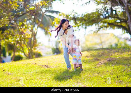 Mother and son in sunny park. Loving Asian family playing outdoor. Mom holding little baby boy. Young woman and adorable child play and laugh. Stock Photo