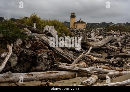 Driftwood piles up along Bullards Beach at Bandon, Oregon with Coquille Lighthouse in the background. Stock Photo