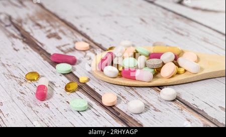 Vitamin capsules in a wooden spoon on a colored background. Pills served as a healthy meal. Drugs, pharmacy, medicine or medical healthycare concept. Stock Photo