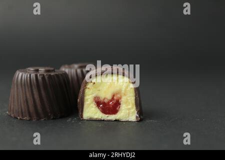 Chocolate case candy filled with mango, passion fruit, cherry, raspberry with yellow and red filling on a black background with space for text and cop Stock Photo