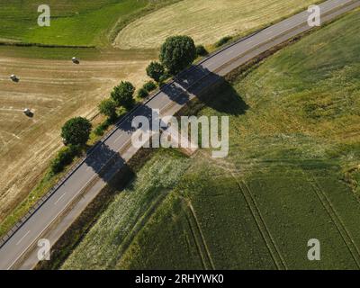 Drone view of a road in the landscape between mowed grass fields and trees Stock Photo