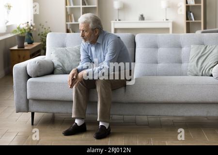 Sad old grey haired man sitting alone on home sofa Stock Photo