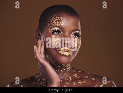 Gold, glitter flake and black woman beauty with makeup and luxury in studio  with sparkle cosmetics. Brown background, smile and female model with  golden paint for skin glow and creative facial shine