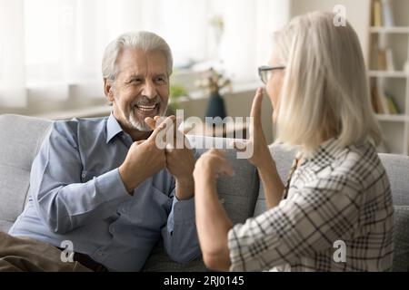 Positive senior husband with hearing disorder, disability talking with hands Stock Photo