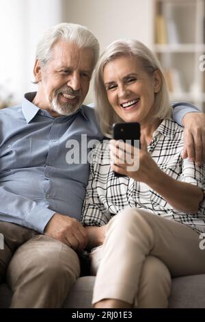 Cheerful old retired husband and wife using smartphone together Stock Photo