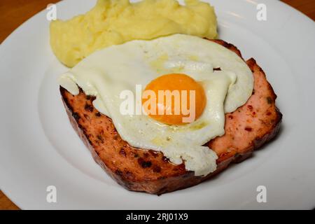 Pan-Fried Spicy Leberkase with Fried Egg Sunny Side Up and Mashed Potatoes on a White Plate Stock Photo