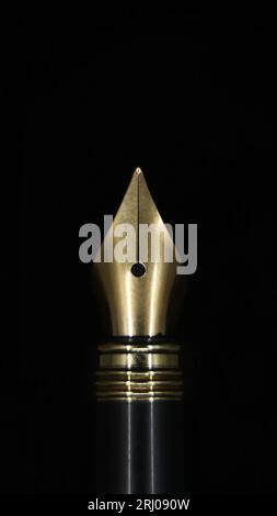 closeup macro shot of the gold tip of a luxury fountain ink pen used for calligraphy isolated in a black background Stock Photo