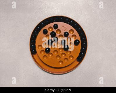 a brain teaser puzzle game played in a wooden solitaire board with marbles or goli balls called brainvita isolated Stock Photo