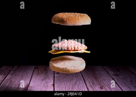 Delicious burger with floating ingredients on the wood table on the black background. Burger and food photo Stock Photo