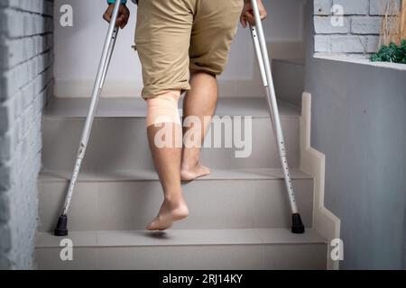 Closeup leg young asian man walking on stair with crutch at home, close-up man walking while bandage with leg, rear view, medical and lifestyle concep Stock Photo