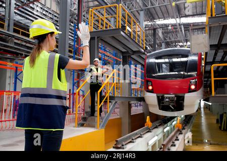 Young caucasian engineer woman or worker signal while engineer man checking electric train for planning maintenance in station, transport and infrastr Stock Photo