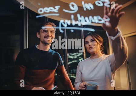 Two business professionals have a late-night discussion in an office, collaborating and brainstorming behind a glass wall. Financial analysts working Stock Photo