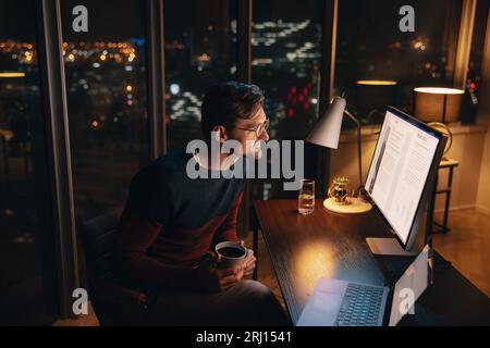 businessman works late at his home office, planning and managing a project. Professional man sitting at his desk with focus and dedication, looking at Stock Photo
