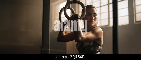 Exercising woman holding gymnast rings. Female taking rest after