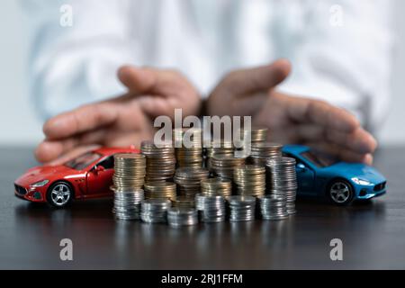 Close-up Of A Person's Hand Protecting Increasing Stacked Coins And Blue Car. Saving money for car concept, trade car for cash concept, finance concep Stock Photo