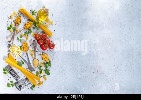 Various dried  spaghetti, noodles, pasta  set in spoons on white table background. Different shapes types raw italian pasta with herbs, olive oil, tom Stock Photo