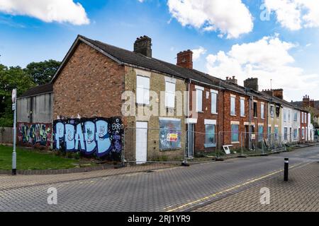 A row of burnt out and derelict terraced houses in the North of England with boarded up windows, doors and fire damaged roofs awaiting demolishion and Stock Photo
