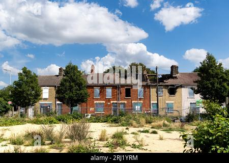 A row of burnt out and derelict terraced houses in the North of England with boarded up windows, doors and fire damaged roofs awaiting demolishion and Stock Photo