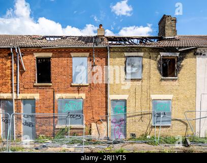 A row of burnt out and derelict terraced houses in the North of England with boarded up windows, doors and fire damaged roofs awaiting demolition Stock Photo