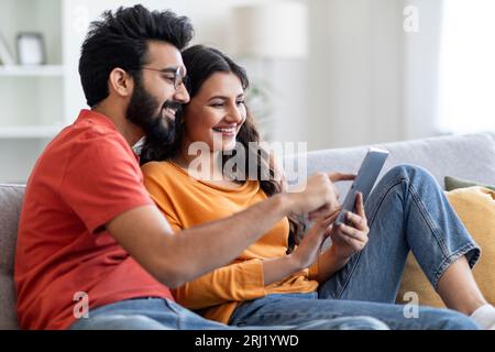 Technologies For Leisure. Happy Indian Spouses Using Digital Tablet At Home Stock Photo