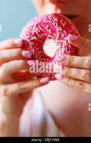 Donut with pink glaze and colored powder in a woman's hand.  Stock Photo