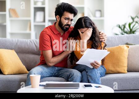 Financial Problems. Portrait Of Depressed Indian Couple Reading Documents At Home Stock Photo