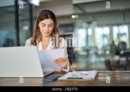 Busy mid aged business woman working in office with laptop and documents. Stock Photo