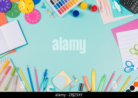 Back to school background. Colored pencils, markers, books, notebooks, pens, watercolor paint, scissors, math fractions, calculator on pastel green Stock Photo