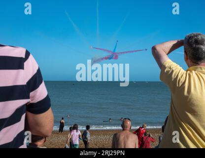 People watch from Eastbourne beach as the world famous RAF display team The Red Arrows fly past the seafront at the annual Eastbourne Airbourne, an in Stock Photo