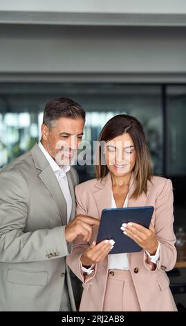 Two professional executive business colleagues using tablet standing in office. Stock Photo