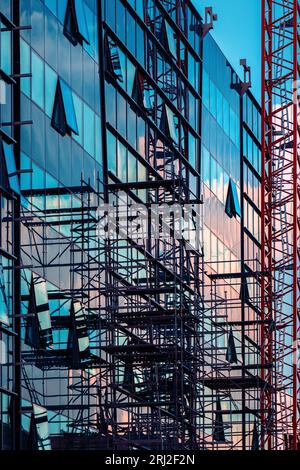 Reconstruction of modern office building with glass facade, construction site with scaffolding and crane forming abstract geometrical pattern, selecti Stock Photo