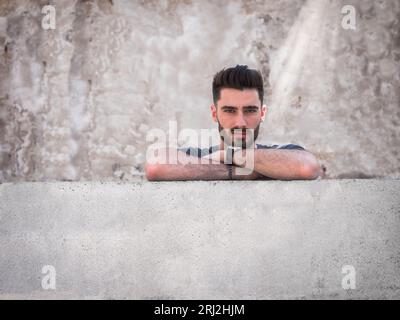 Photo of a confident man leaning against a wall with his arms crossed Stock Photo