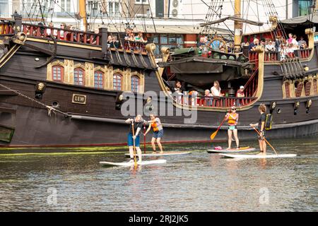 Paddleboarding in Gdansk. People on paddleboards passing by the Lew pirate galleon river cruise ship on Motlawa River in the Old Town of Gdansk Poland Stock Photo