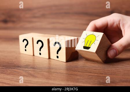 Idea concept. Woman putting cube with illustration of light bulb to other ones with question marks on wooden table, closeup Stock Photo