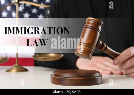 Immigration law. Judge with gavel at white wooden table near flag of United States, closeup Stock Photo