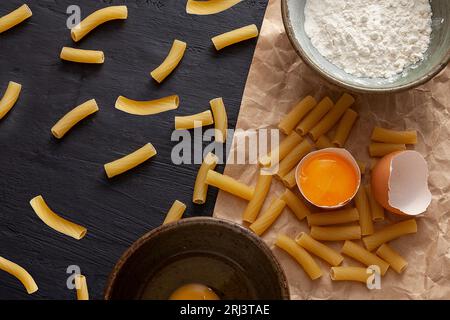 A variety of fresh pasta with flour and eggs spread out on a wooden table, ready for preparation Stock Photo