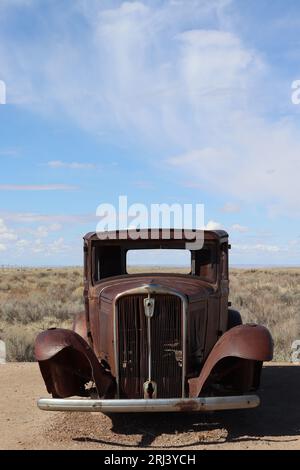 An abandoned vintage car sitting in the middle of a barren desert Stock Photo