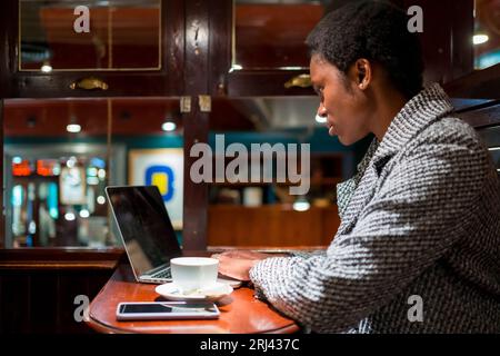 A shallow focus of a young black woman working on her laptop from a coffee shop Stock Photo