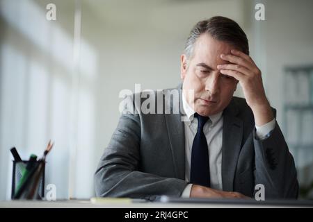 Depressed pensive businessman sitting at desk in his office Stock Photo
