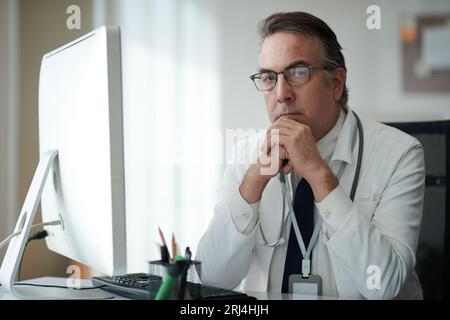 Portrait of serious head of clinic sitting at desk and looking at camera Stock Photo