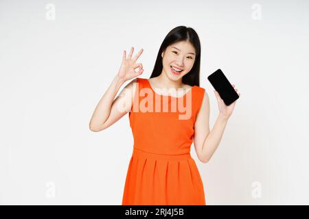 Young woman holding smartphone and shows OK sign on white background. Stock Photo