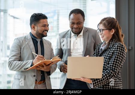 A multiracial group of business people is discussing work while standing in a company corridor together. diverse colleagues, Asian, African American, Stock Photo