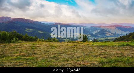sunrise over uzhanian pass. carpathian rural landscape in summer. hay drying on the meadow. village down in the valley Stock Photo