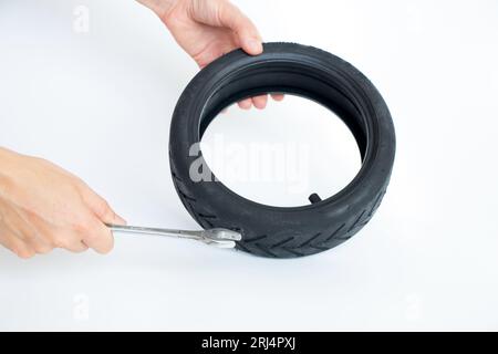 Tire of an electric scooter and a hand holds a wrench on a white background, replacement and repair of electric scooters, replacement of a wheel on a Stock Photo